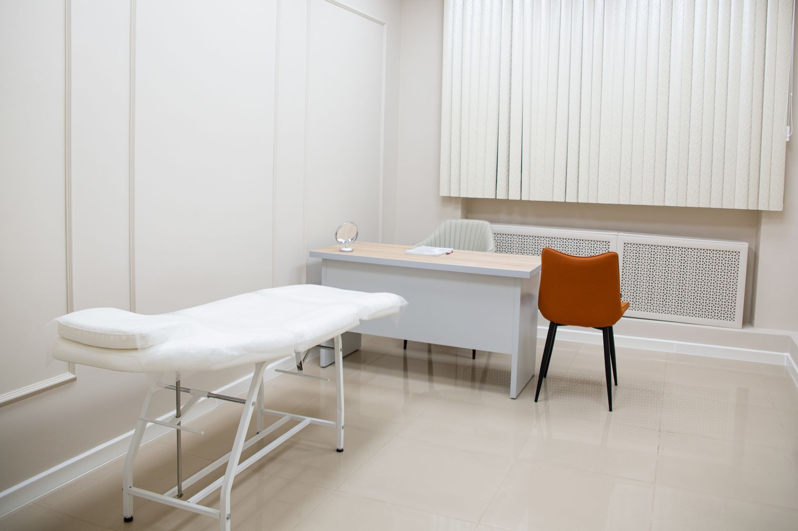 Sala de consultório particular clara, com maca, mesa e cadeiras